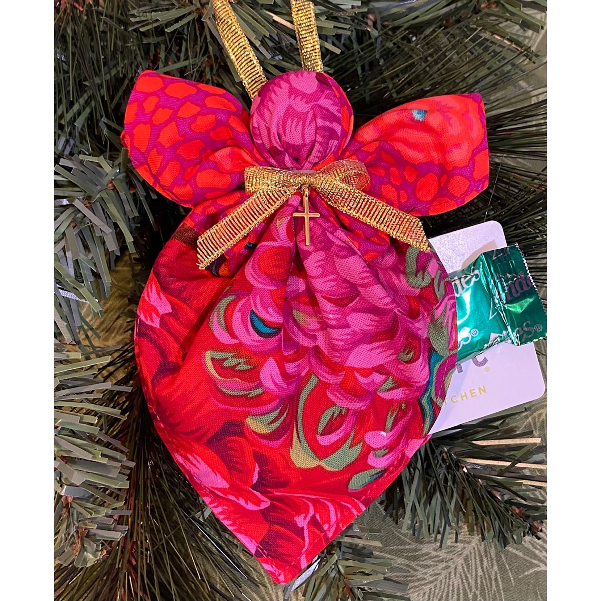 Angel ornament hanging on a tree shows gift card and candy from pocket.