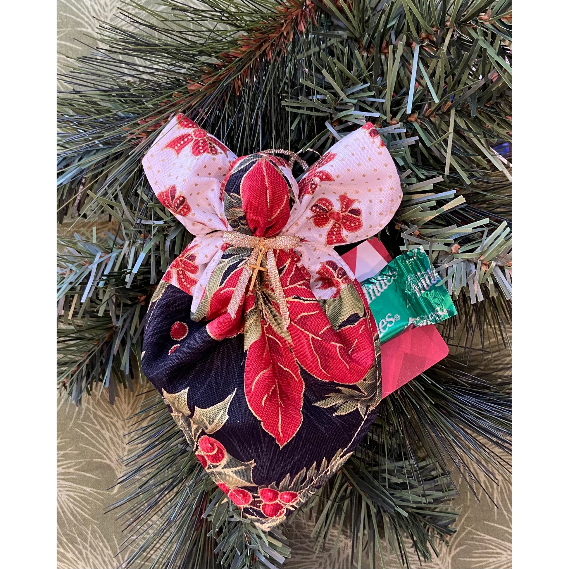 Angel ornament hanging on a tree shows gift card and candy from pocket.