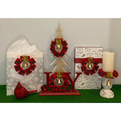 Seasonal display of ways to use the completed Christmas Wreaths ornaments. Shown as decoration on a gift bag, on a small wooden tree, in the O of Joy, on a gift box and around the base of a candle.