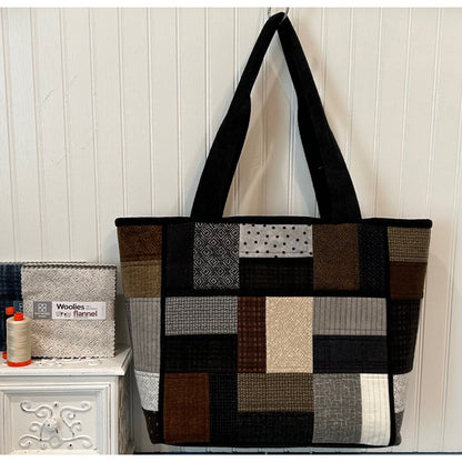 Classy tote bag in black, brown, and gray fabric in patched blocks with black handle and piping around edges and two pockets in middle.