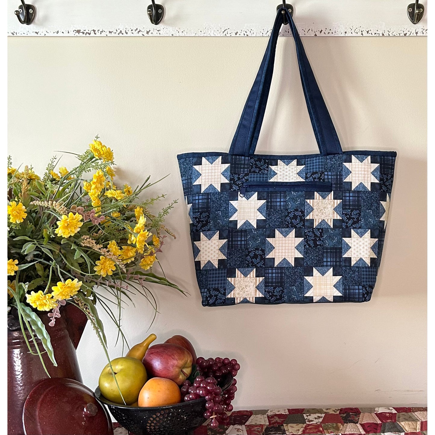 Beautiful tote bag hanging from a hook in the kitchen. Bag features stars on blue fabric with a zippered pocket in the middle.