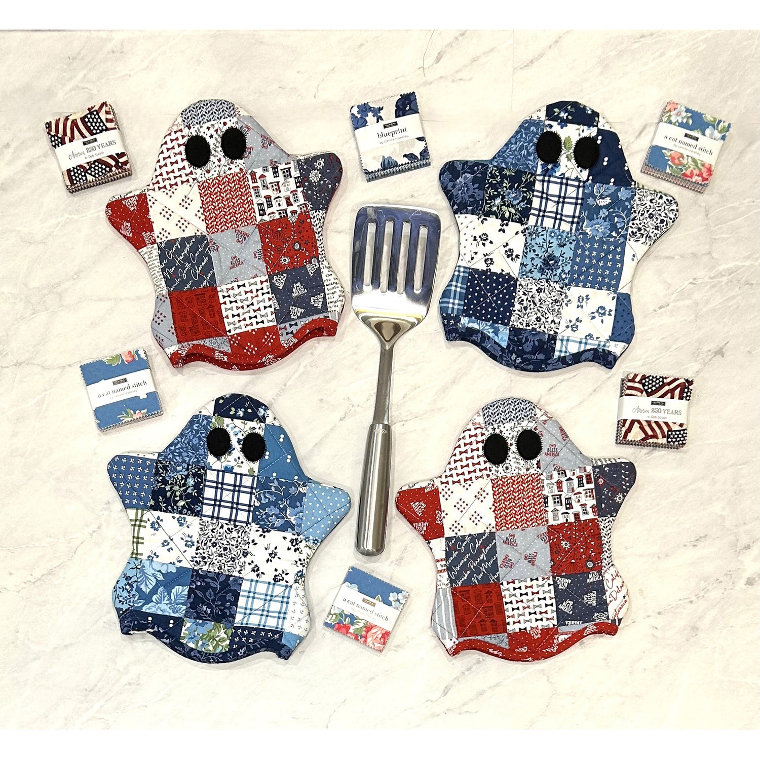 Set of patchwork ghost-shaped potholders with a spatula on a white background