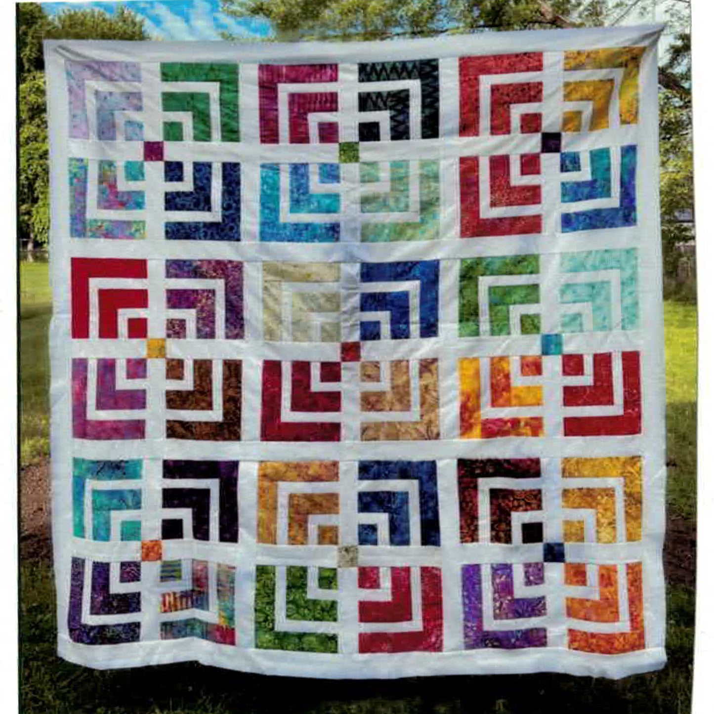 A vibrant quilt featuring an array of multicolored squares which showcases small to larger V of color sort of like the symbol for WiFi.  In between some of them are colorful squares to give the grouping of four a feel of being all one.