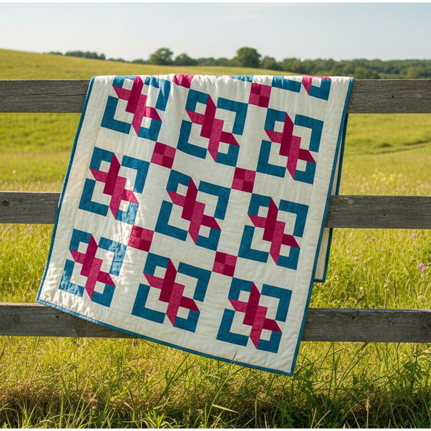 Quilt with geometric pattern draped over a wooden fence in a grassy field