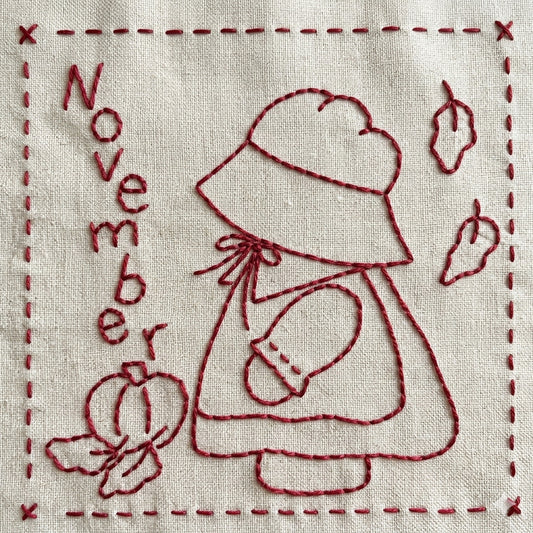 Sunbonnet Sue redwork embroidery design for November featuring Sunbonnet Sue in her pilgrim outfit picking a pumpkin as leaves fall.