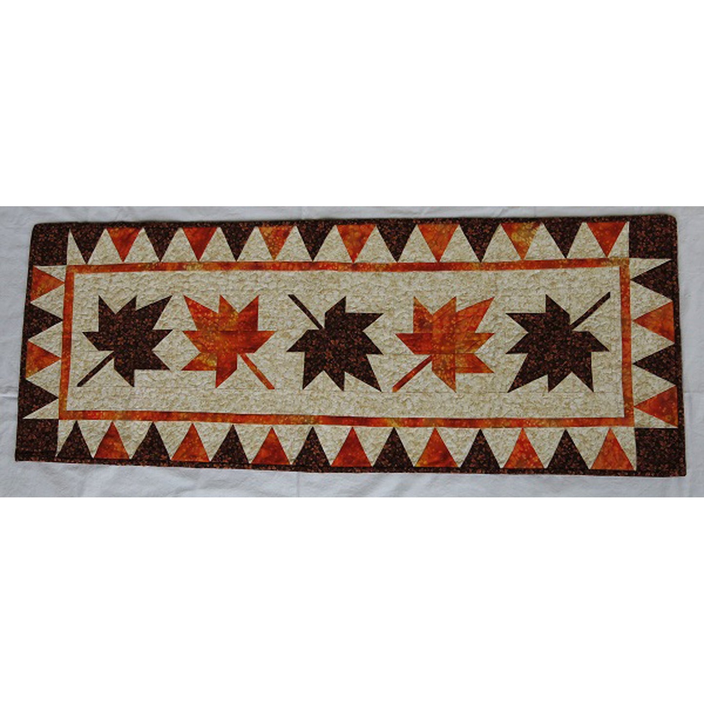 Autumn table runner with falling maple leaves down the middle in orange and brown.