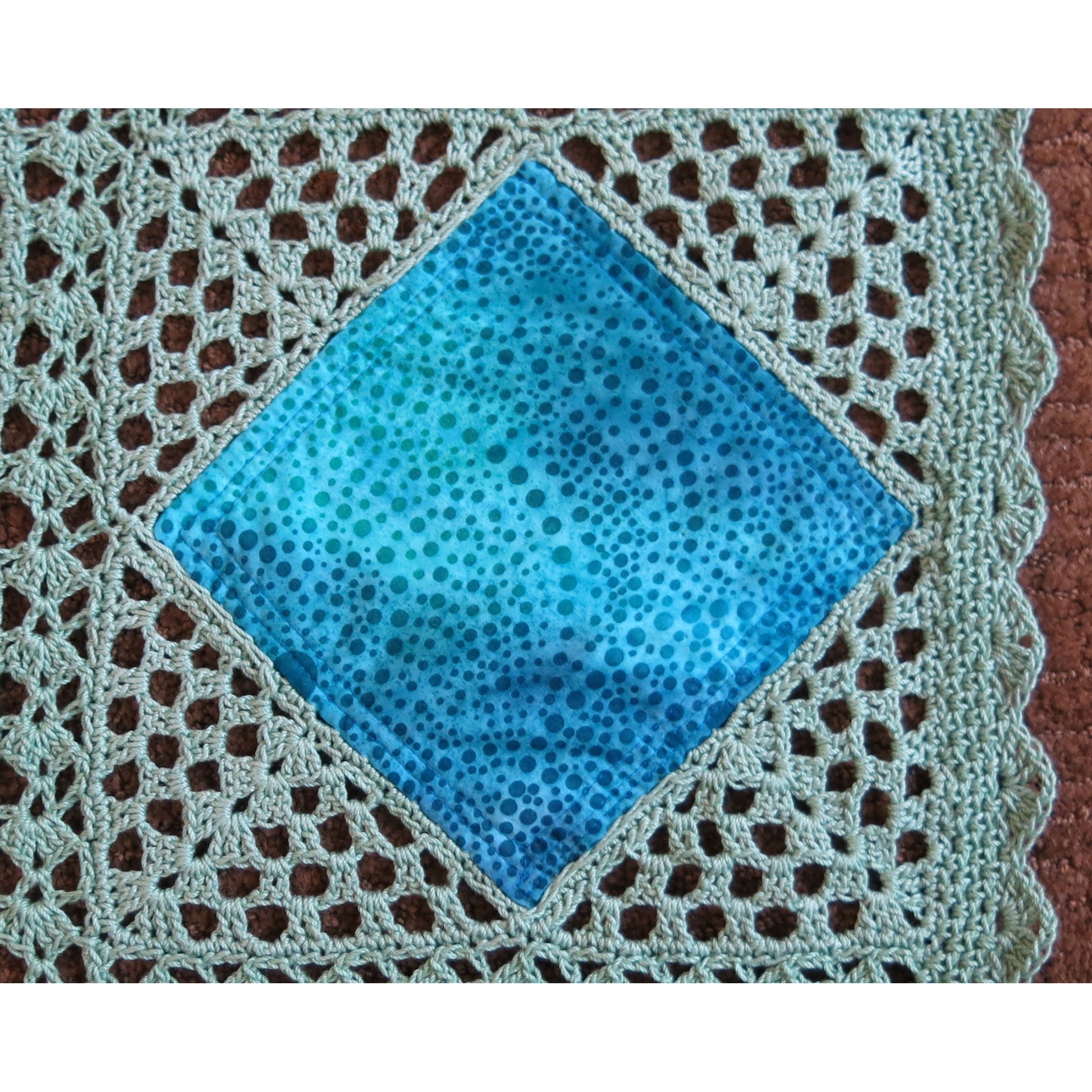 Close up of crocheted quilt, showing diamonds of blue fabric with crochet around it to form a block.