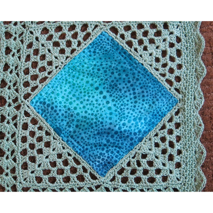 Close up of crocheted quilt, showing diamonds of blue fabric with crochet around it to form a block.