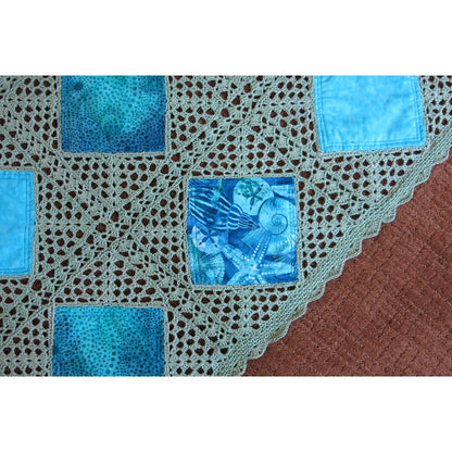 Beautiful quilt features diamonds of blue fabric crocheted together in a neutral cream thread. Close up shows a few blocks so you can see the beautiful detail.