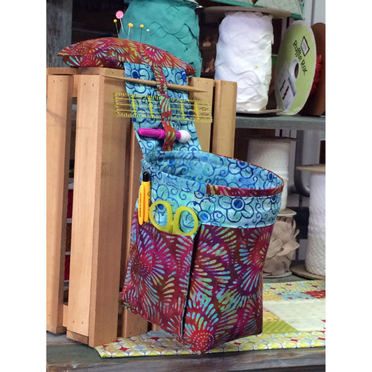 Colorful scrap catcher basket shown with pin cushion on top and pockets for scissors and pen and place between pin cushion and basket for tools like small ruler and seam ripper.