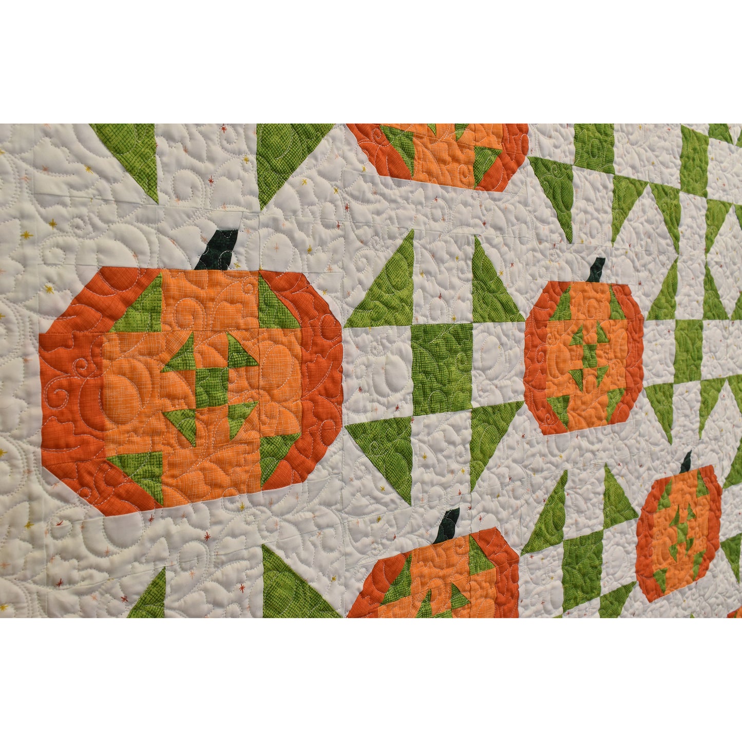 Closeup image of Pumpkin Barn Dance quilt showing two pumpkins with design inside in green along with similar design between pumpkins in green and showcasing quilting with pumpkins and vines.