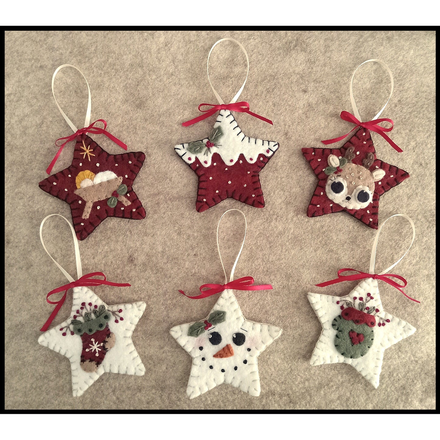 Six festive star wool felt ornaments. Six different designs include: manger, reindeer, stocking, mitten, snowman face and snow covering a red star.