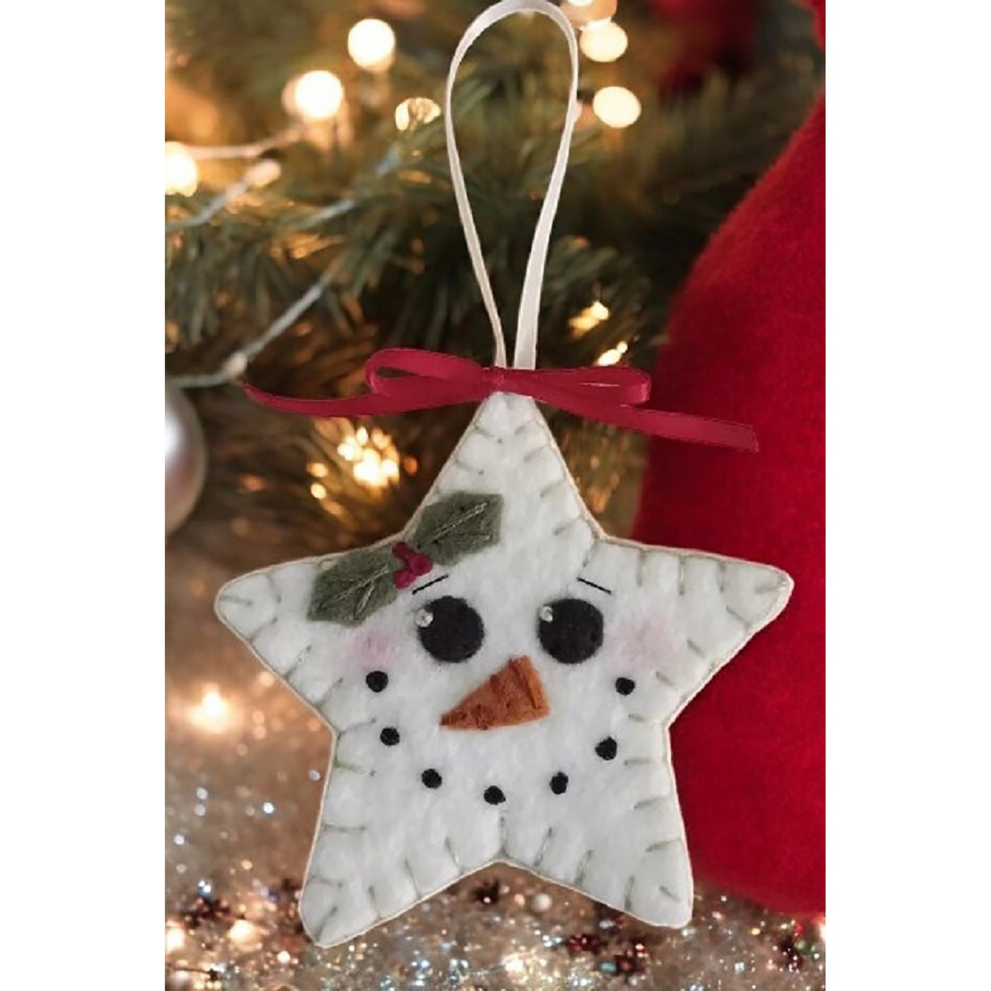 Close up of a star ornament with snowman face including carrot nose. White ribbon hanger and red ribbon finish off the look.