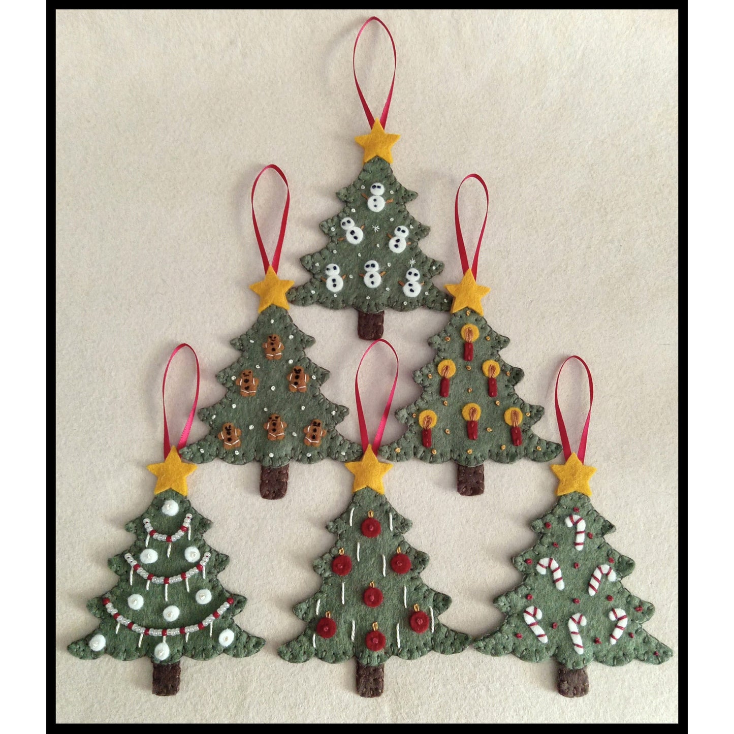Set of five Christmas tree-shaped decorations with red ribbons and yellow stars on a beige background.