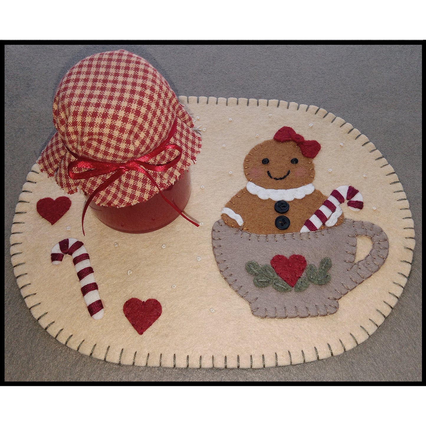 Adorable mug rug made from wool felt with a cute gingerbread lady with bow and candy cane in a tea cup with a heart on it.