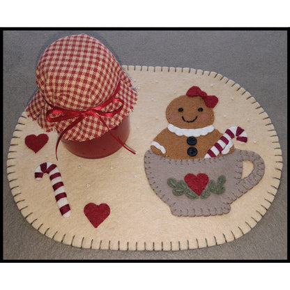 Adorable mug rug made from wool felt with a cute gingerbread lady with bow and candy cane in a tea cup with a heart on it.