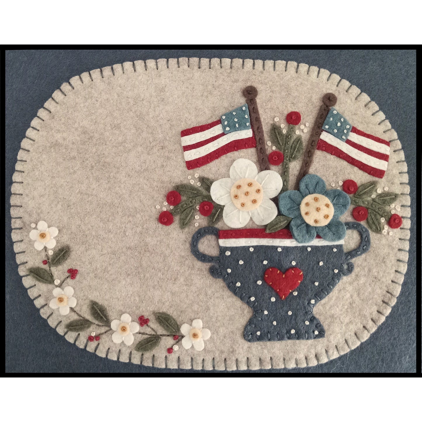Wool candle mat is a heirloom-style pattern features a lovely vase filled with pretty flowers and two American flags.