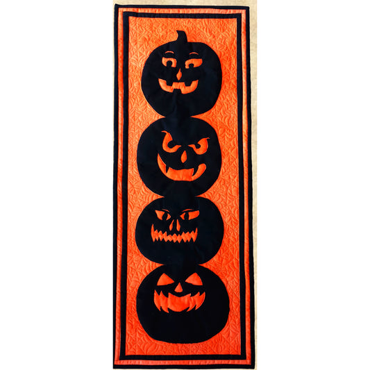 Spooky quilted table runner in orange with four black Jack o'lanterns.