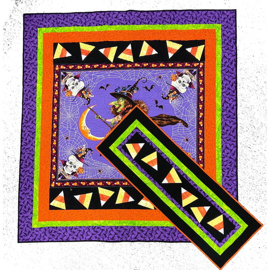 Bright Halloween quilt with witch on a broom and candy corn border. In front is a table runner with bright colors with candy corn.