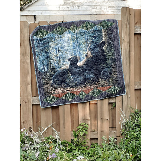 Quilt hanging on a fence featuring an adorable bear and cub.