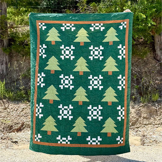 Beautiful winter-themed quilt features pine trees and snow flakes.
