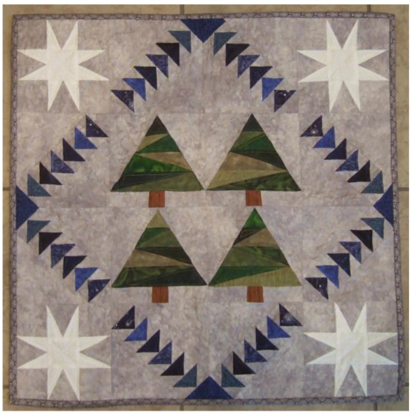 Sweet quilt features four scrappy pine trees in the middle of a diamond of flying geese blocks and white stars or snowflakes in the four corners.
