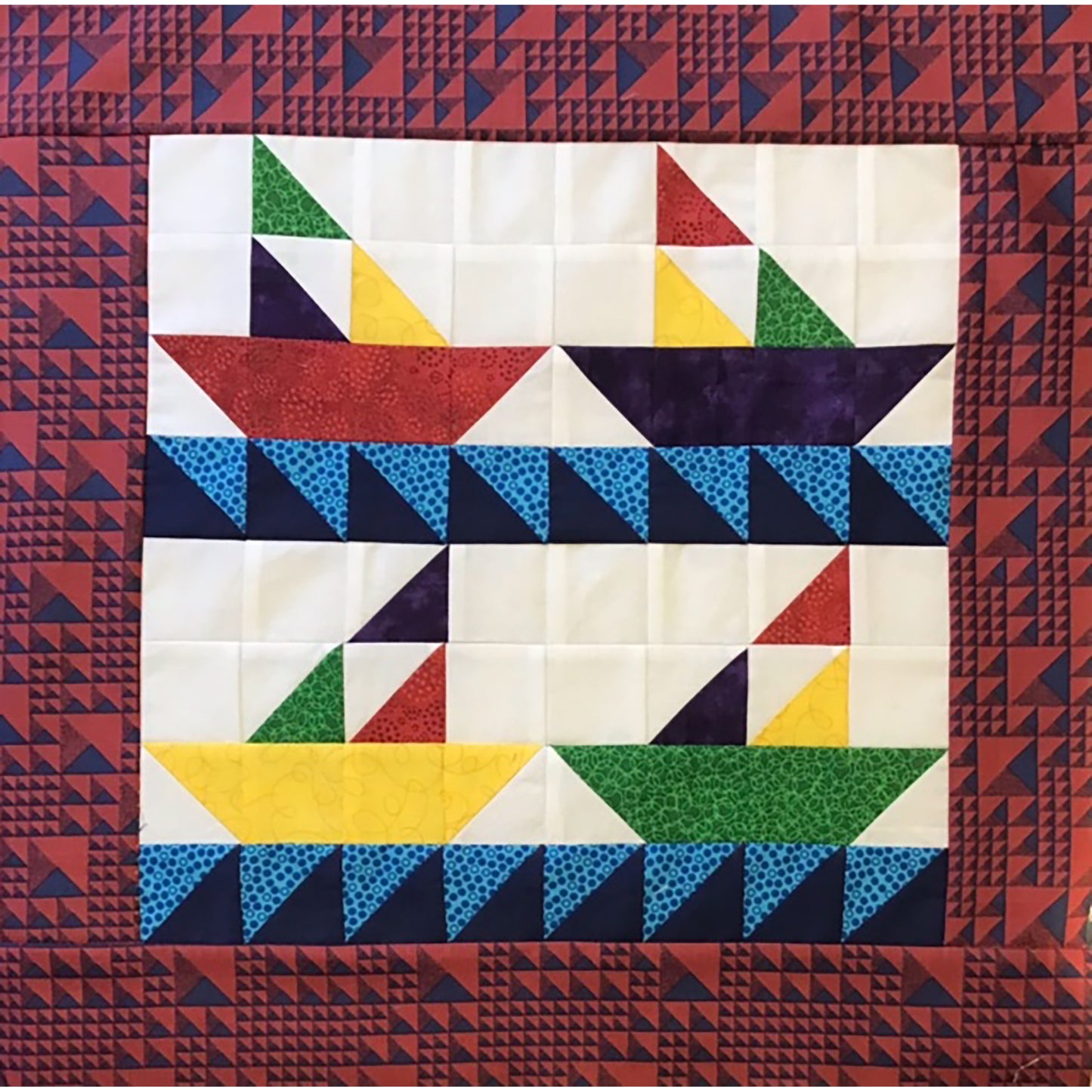 Four pieced sail boats made from bright colored fabrics with blue waves. The top two appear to be heading to the right and bottom two to the left. Their sails are made from three triangles.