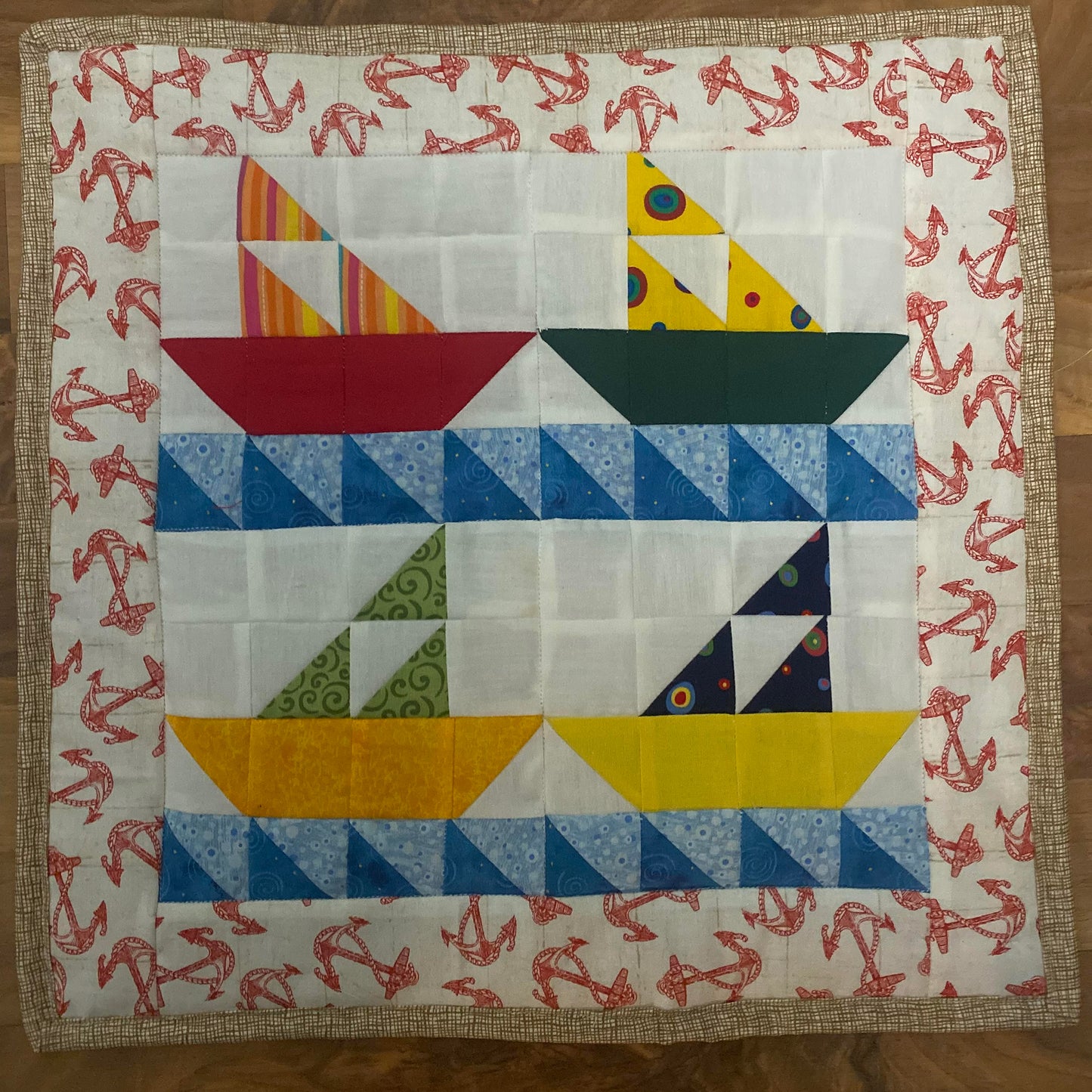 Four pieced sail boats made from bright colored fabrics with blue waves. The top two appear to be heading to the right and bottom two to the left. Their sails are made from three triangles.