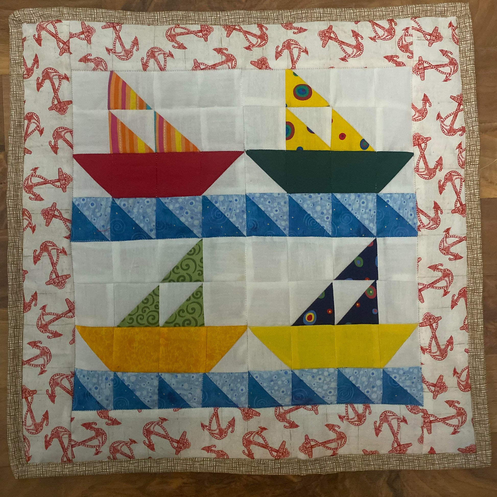 Four pieced sail boats made from bright colored fabrics with blue waves. The top two appear to be heading to the right and bottom two to the left. Their sails are made from three triangles.