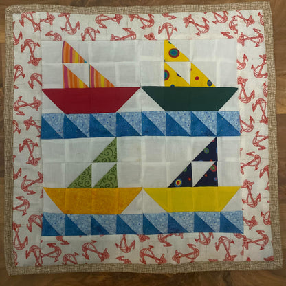 Four pieced sail boats made from bright colored fabrics with blue waves. The top two appear to be heading to the right and bottom two to the left. Their sails are made from three triangles.