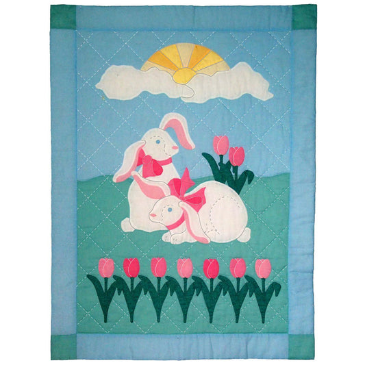 Adorable quilt features two bunnies with ribbons around their necks and a row of tulips. There is a sun in clouds in the sky. So adorable. The bunnies remind me of a stuffed bunny toy.