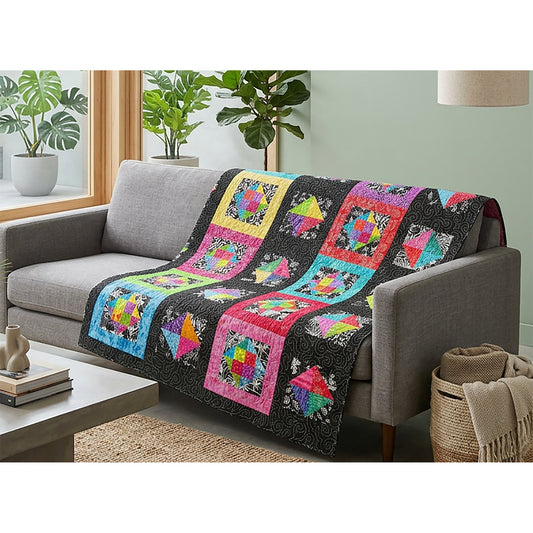 Fun black and white and colorful quilt shown draped on a couch. Quilt features rows of blocks some with black borders and others with bright colored borders. Each block includes a colorful square some in four pieces and others with more. 