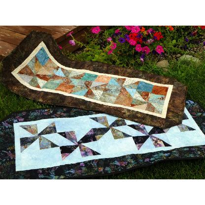 Two quilted table runners with geometric patterns displayed outdoors.
