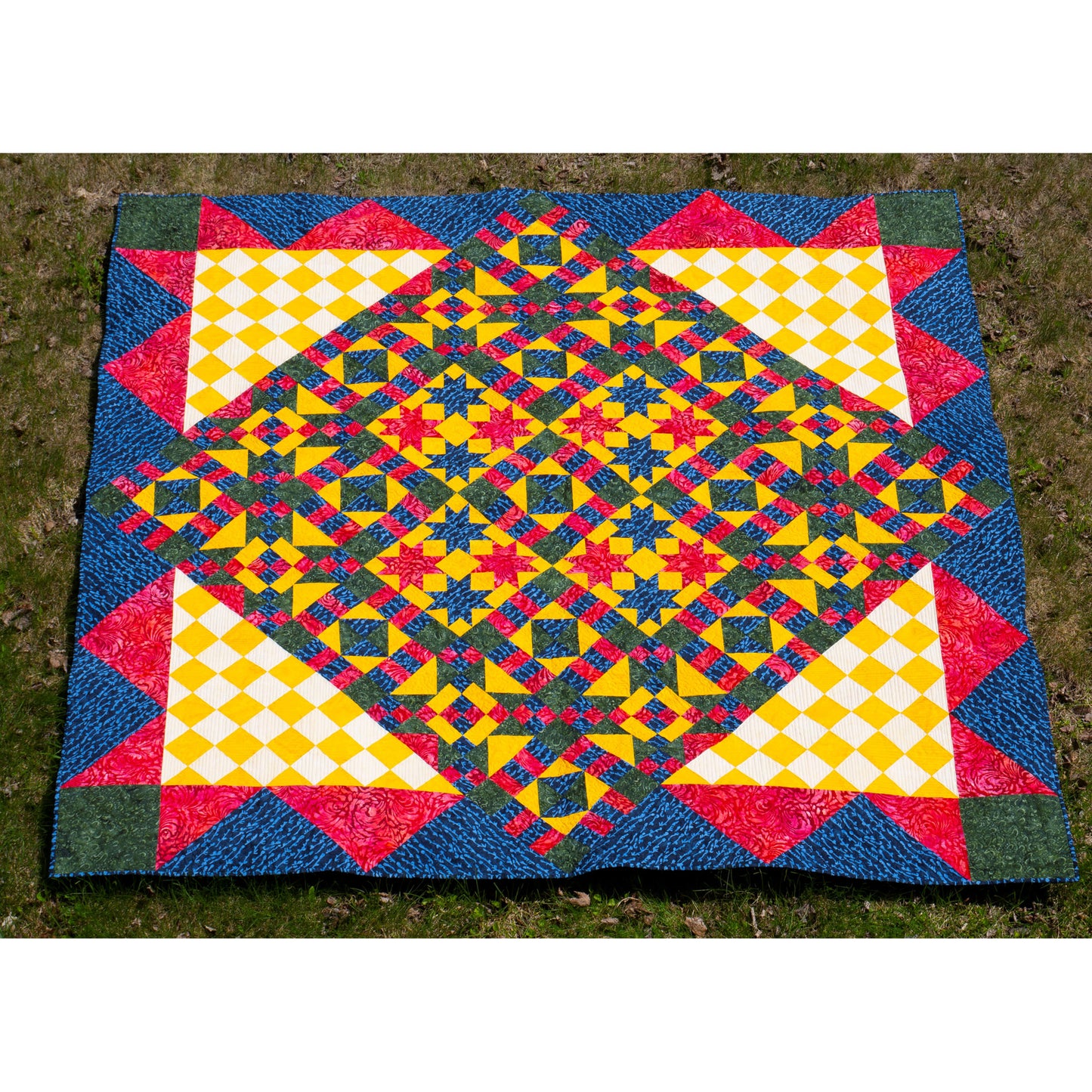 Colorful geometric-patterned quilt on a grassy background