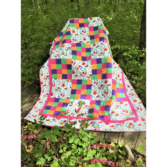 Colorful quilt with floral patterns draped over a tree stump in a forest setting