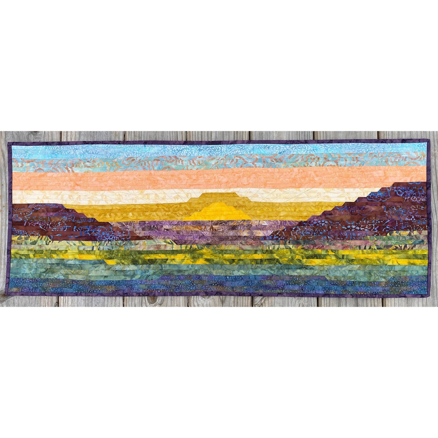 Quilt with landscape design featuring mountains and sky on a white background