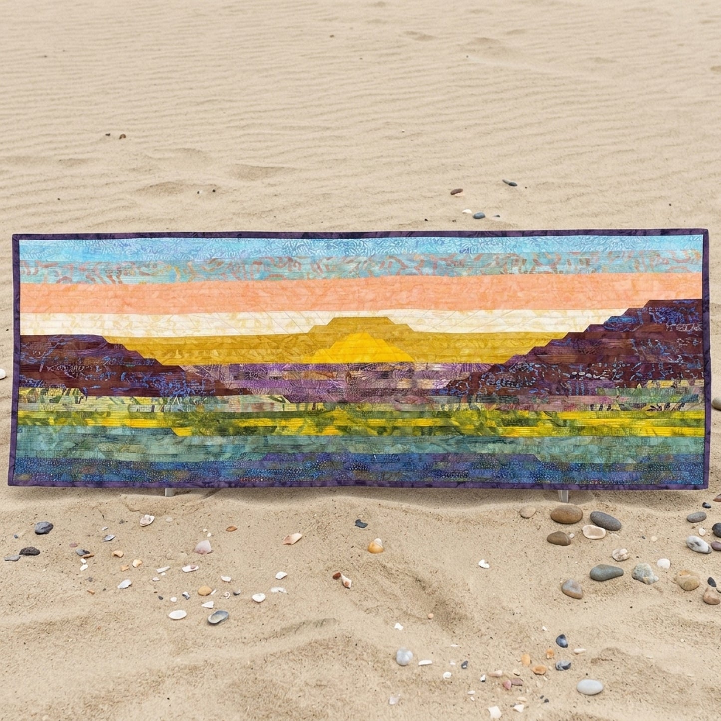Colorful landscape quilt on a sandy surface with pebbles