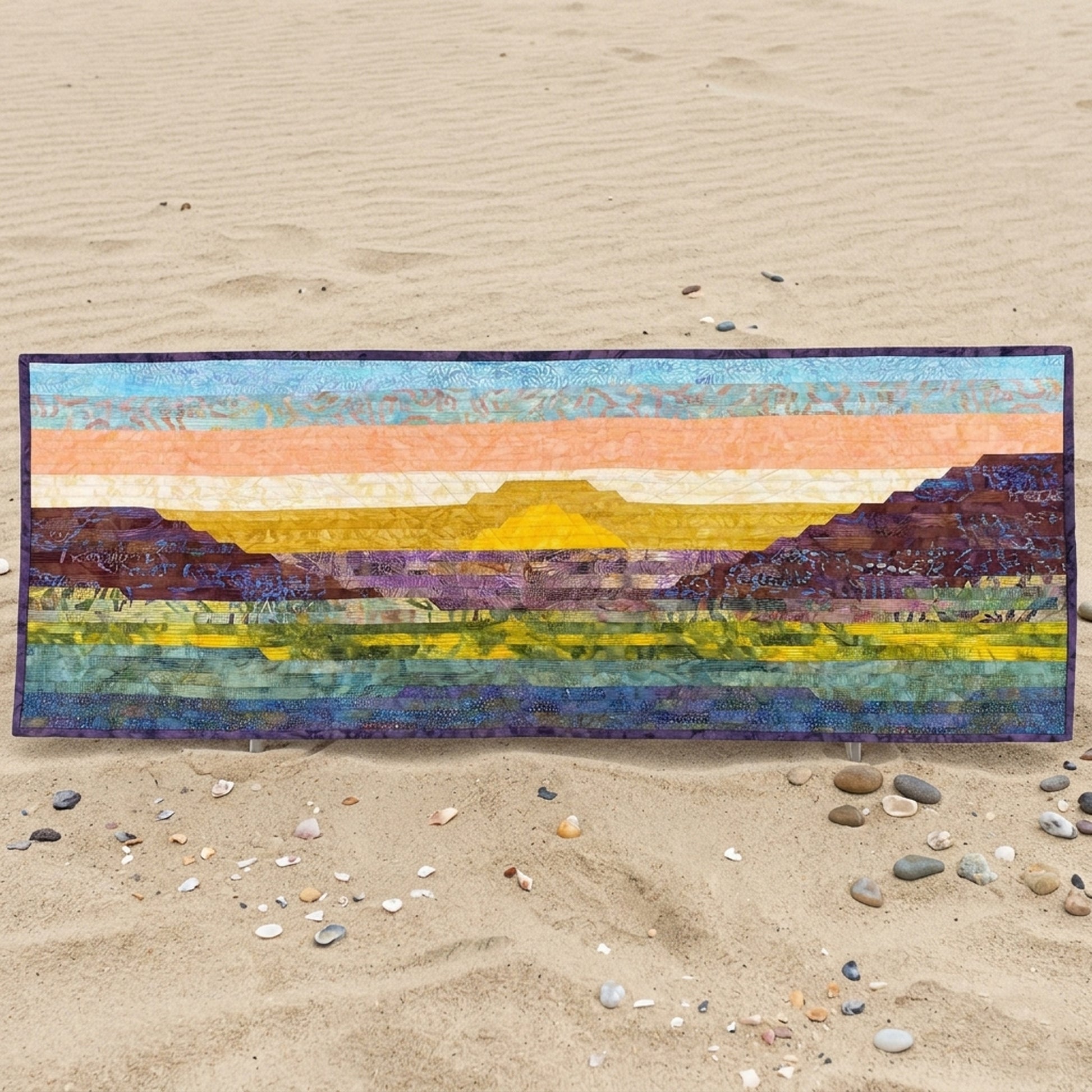 Colorful landscape quilt on a sandy surface with pebbles