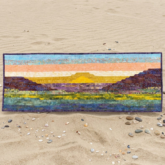 Colorful landscape quilt on a sandy surface with pebbles