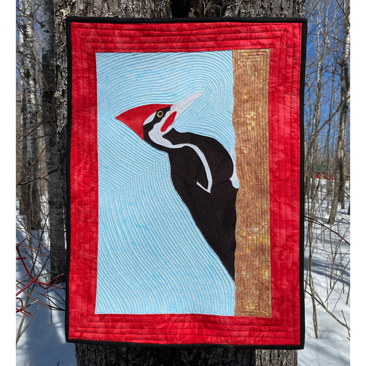 Quilted wall hanging with a woodpecker design in a snowy forest setting