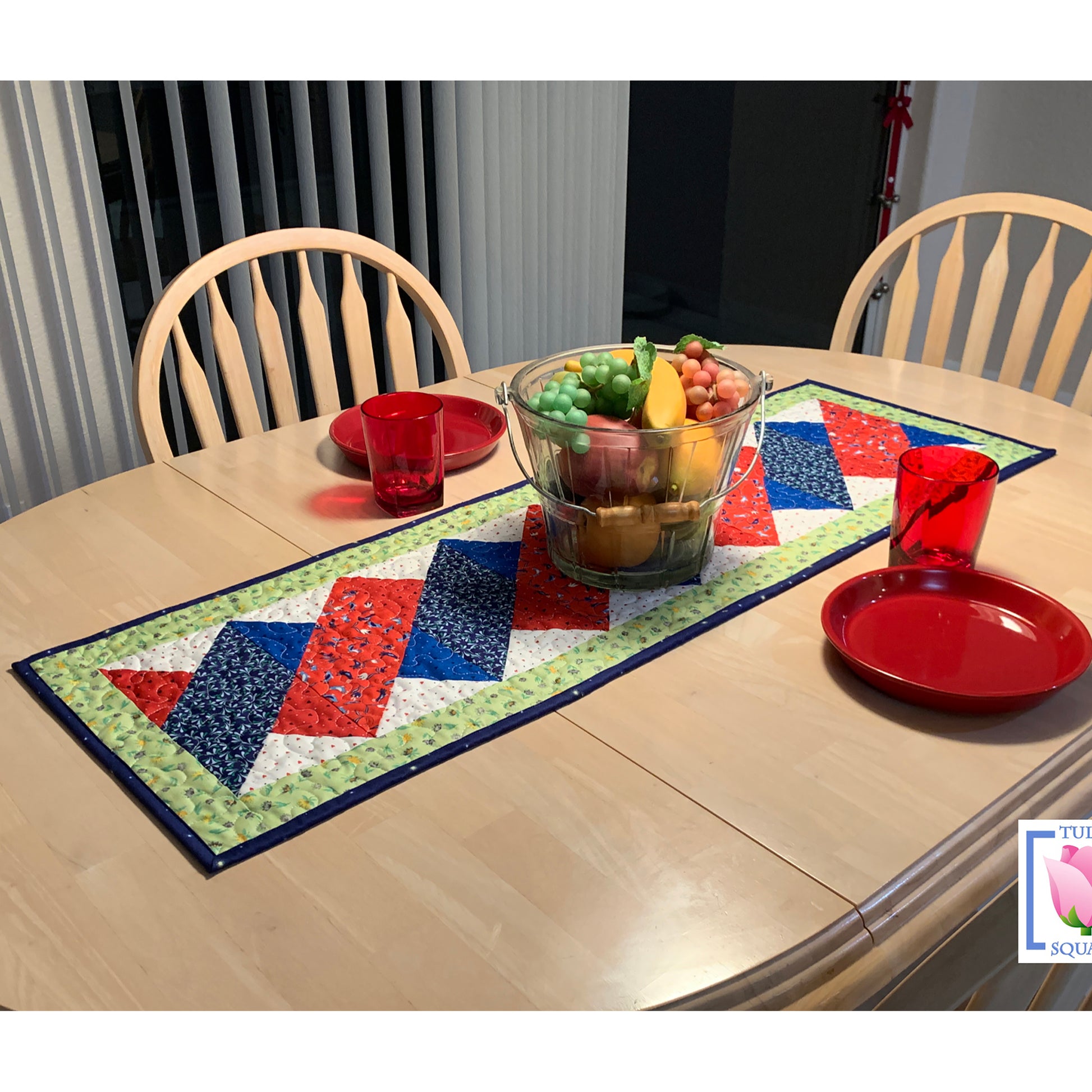 Pretty twist looking table runner with red and blue twist in the middle - shown on a table with a bowl of fruit.