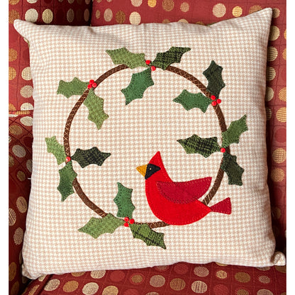 A festive red cardinal pillow adorned with holly leaves, perfect for adding holiday cheer to any space.